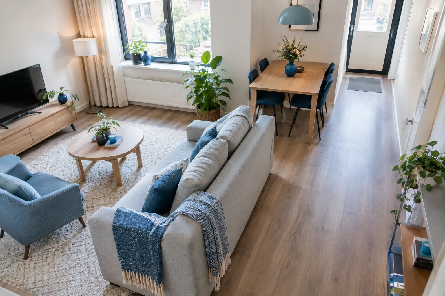 Schuin bovenaanzicht van een lichte woonkamer met een bank tussen zit- en eethoek en een vrije looproute langs de wand